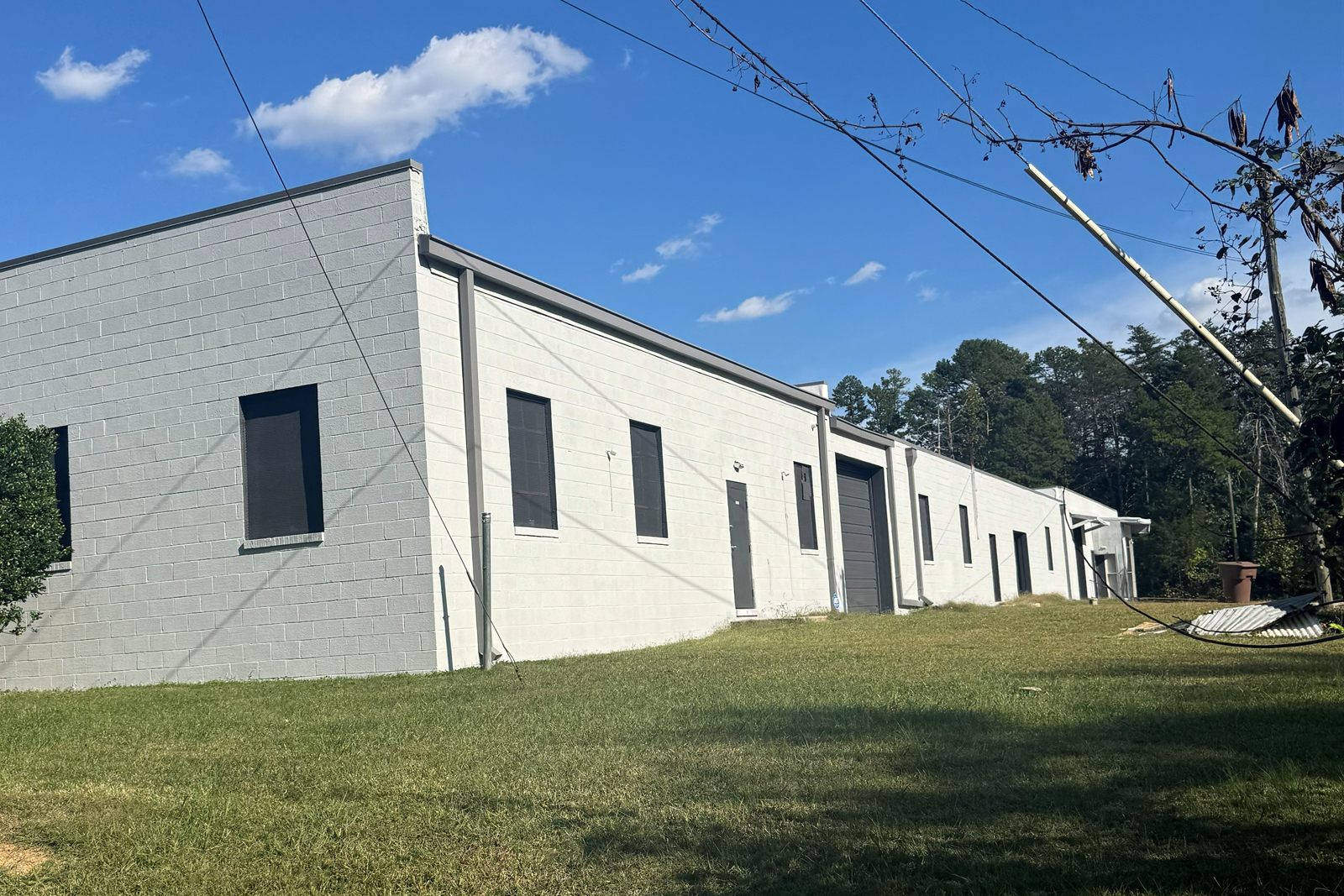 The long side of 314 Mandustry Street, freshly painted white masonry with gray trim and downspouts, dark gray doors and windows, and a drive-in door partway down the building