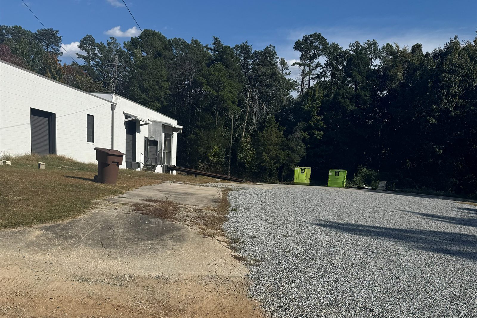 Gravel yard at 314 Mandustry Street beside the end of the white masonry building, backed by a wooded tree line
