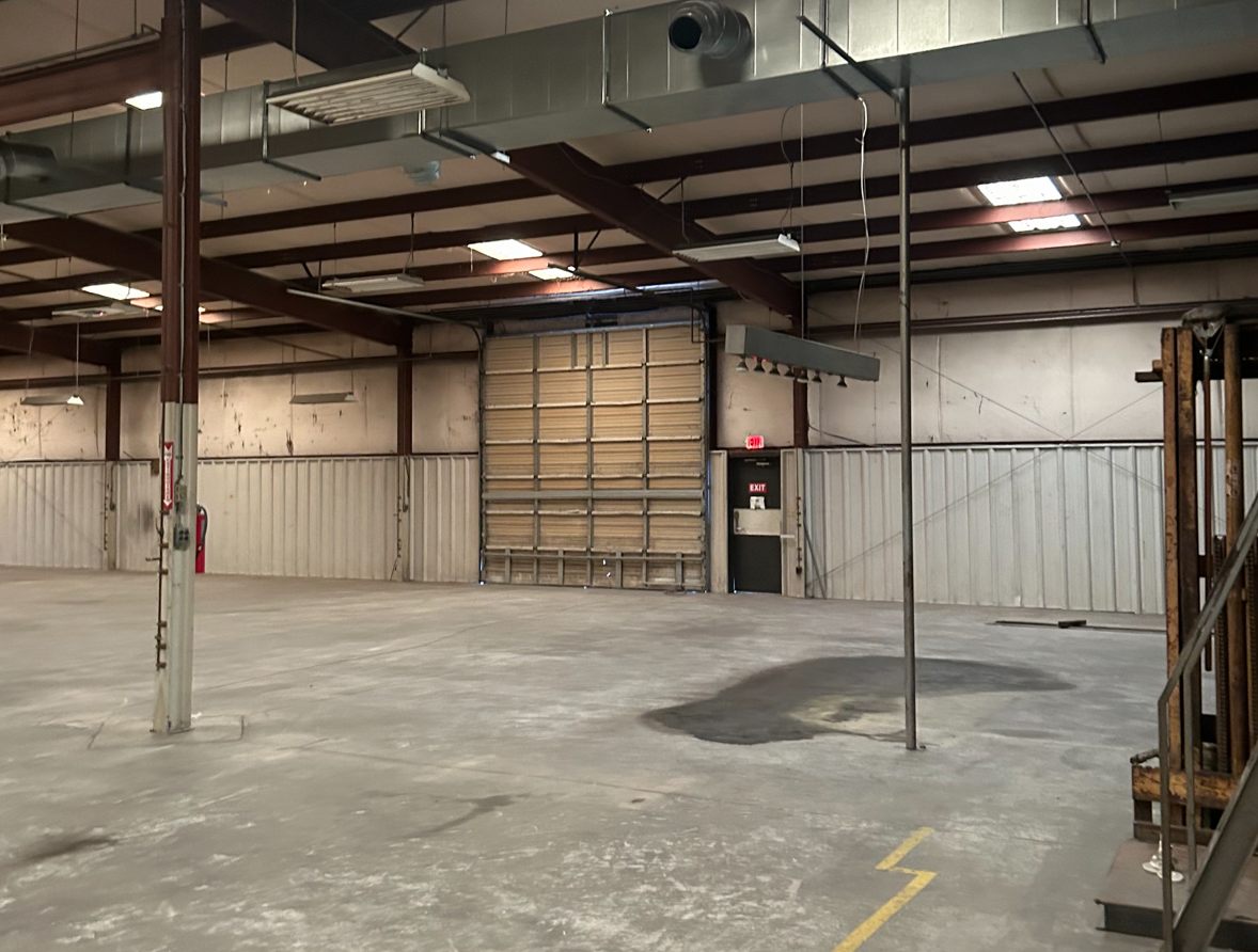 Warehouse at 4475 Technology Drive NW showing a tall sectional drive-in door beside an exit door, metal wainscot walls, ductwork, and steel roof framing