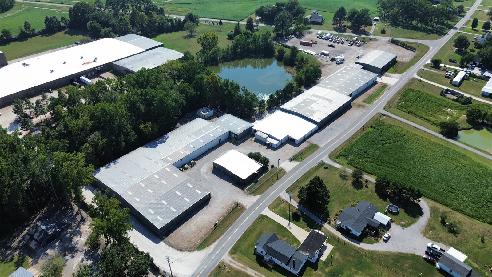 High aerial view over 4734 Potato House Court showing the park's warehouse buildings along the road, the pond behind them, and farmland around