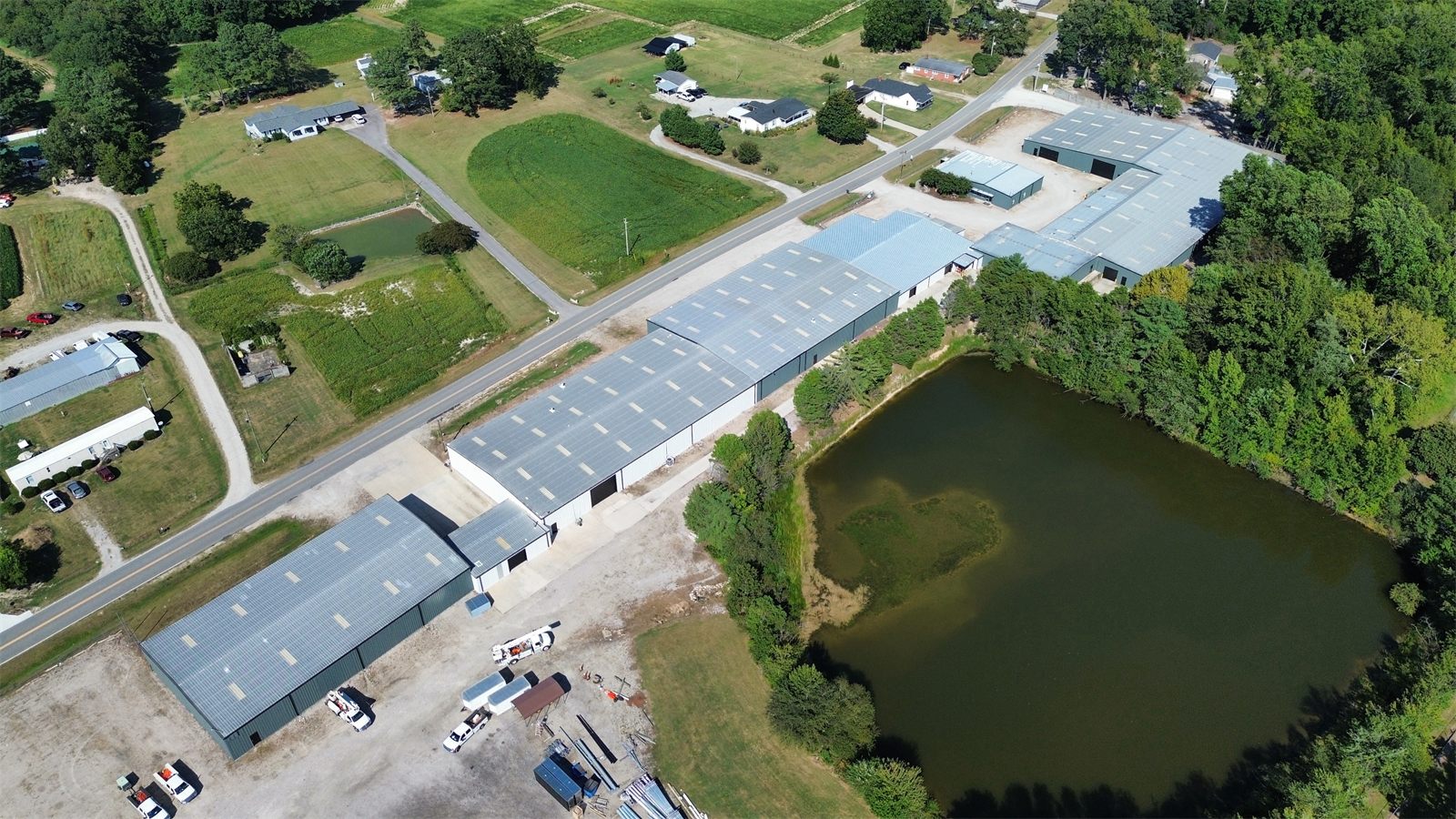Aerial view of the 4734 Potato House Court buildings in a row along the road, with the pond and tree line behind