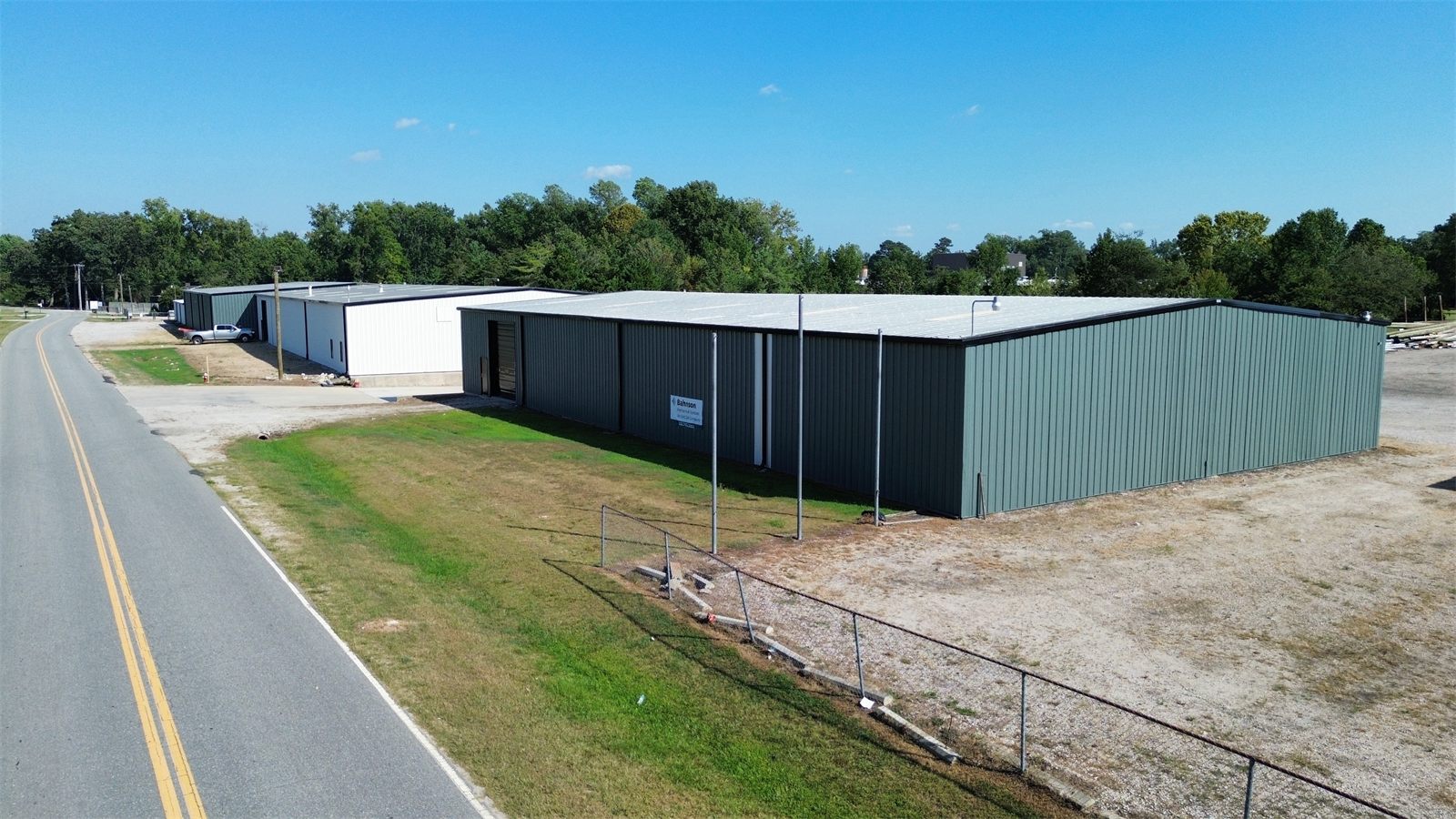 Green metal warehouse at 4734 Potato House Court beside the road, with chain-link fencing along the yard