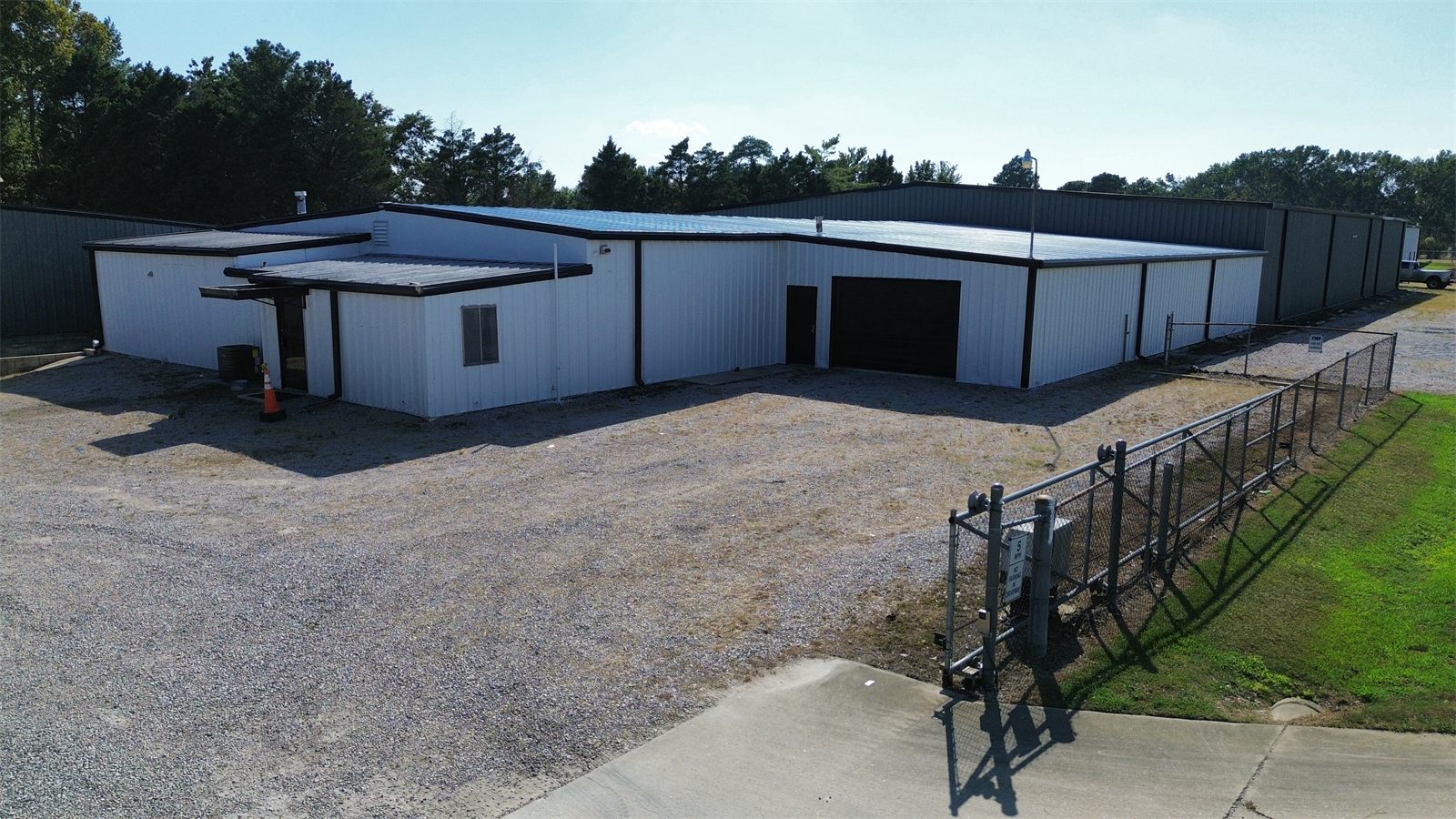 Automated gate and chain-link fence at the gravel yard entrance beside a white metal warehouse