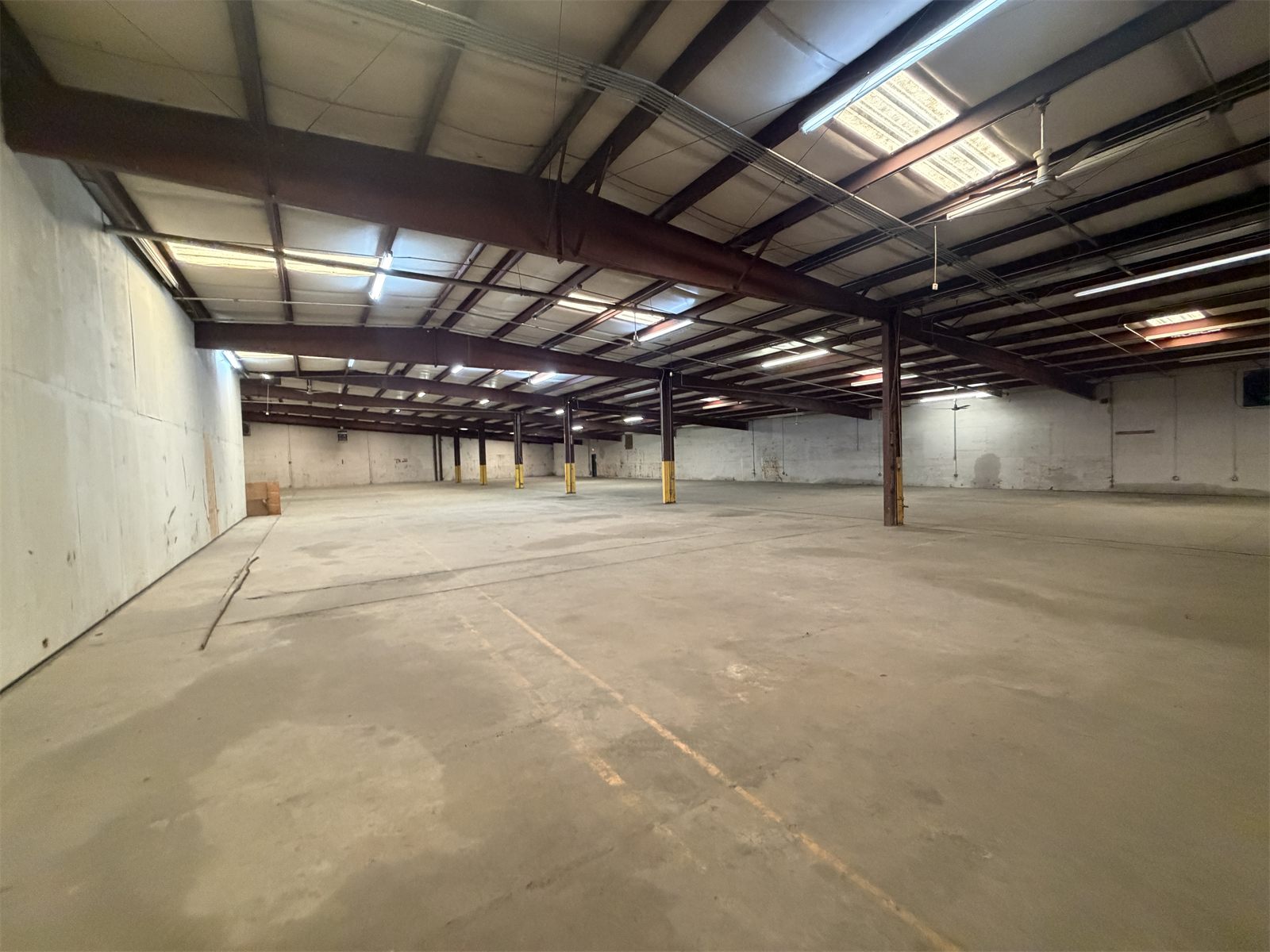 Long, empty clear-span warehouse at 4734 Potato House Court with exposed steel beams, skylight panels, and an open concrete floor
