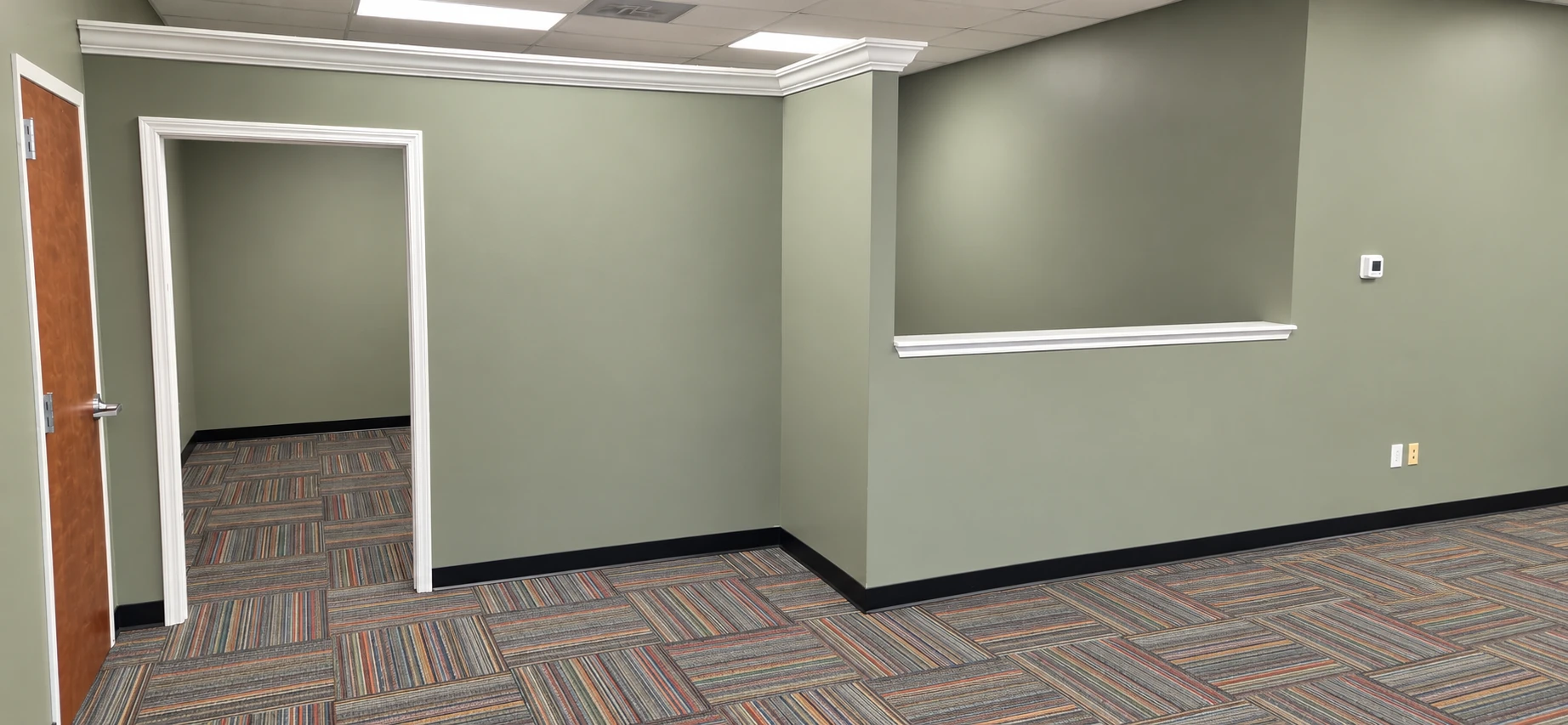 Suite B office area at 7204 Stinson Hartis Road with sage-green walls, white crown molding, carpet tile, a private office doorway, and a reception pass-through window