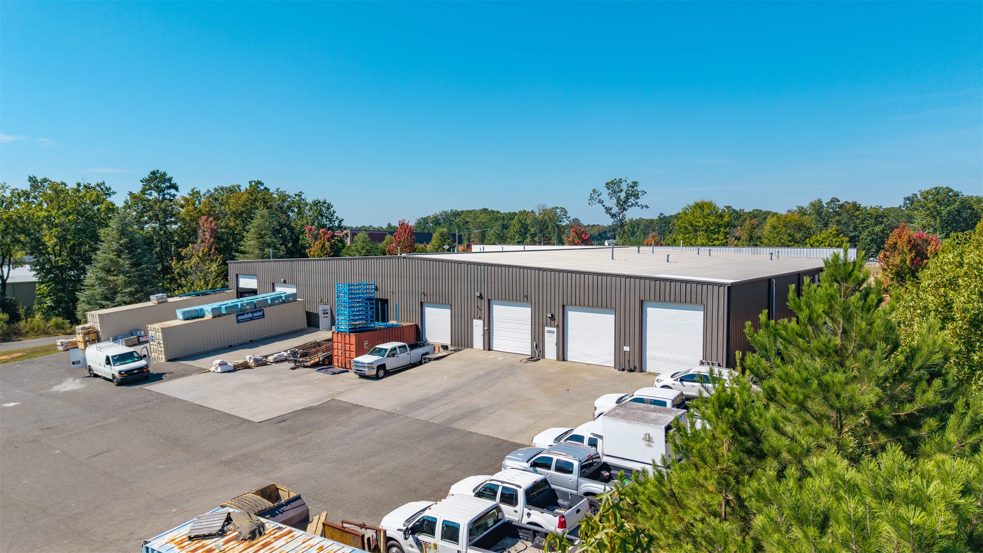Rear of 7204 Stinson Hartis Road with four white roll-up doors on the metal warehouse wall and a wide paved loading court